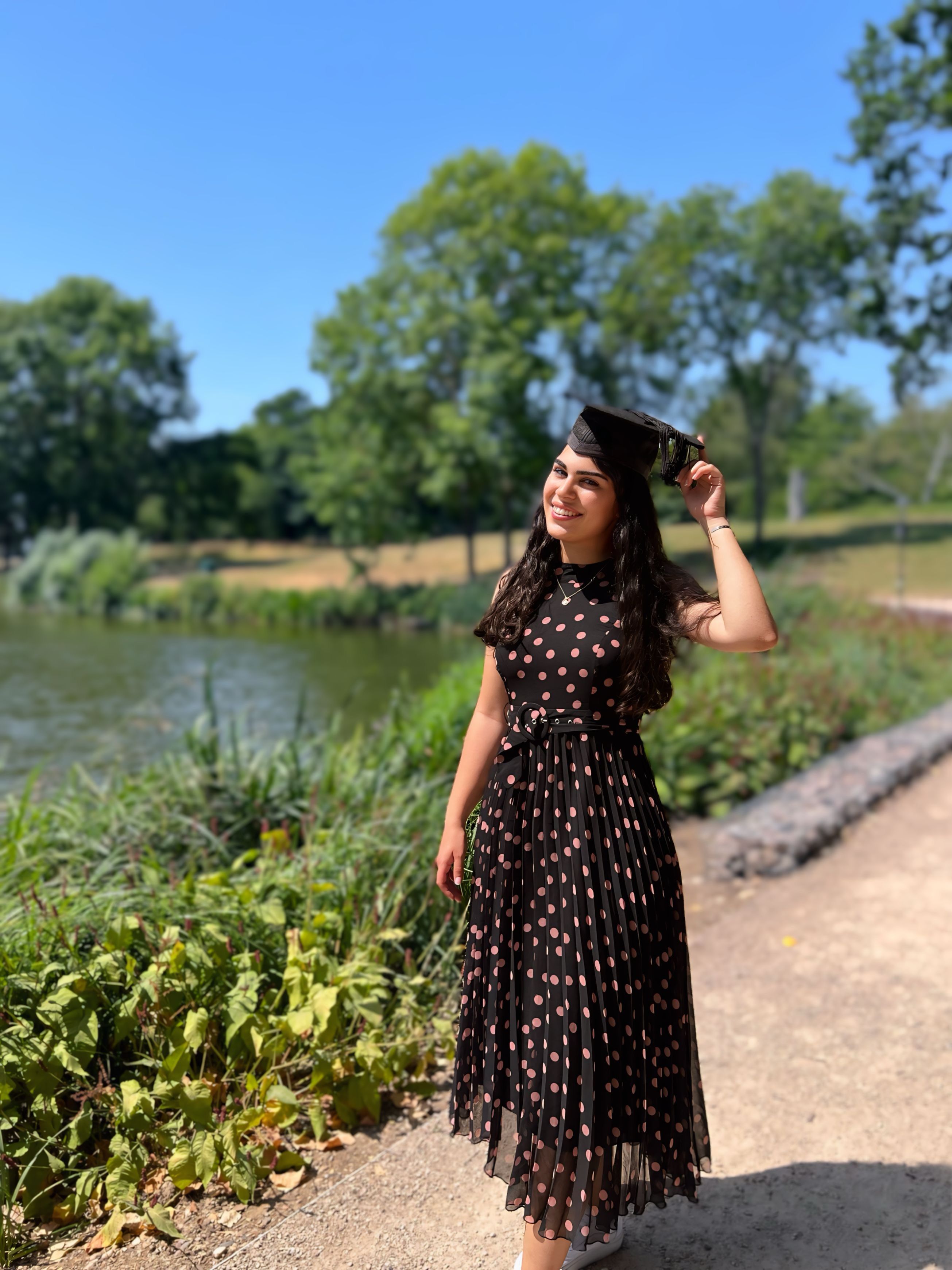 Ela wearing a mortarboard stood by the lake at our Colchester campus
