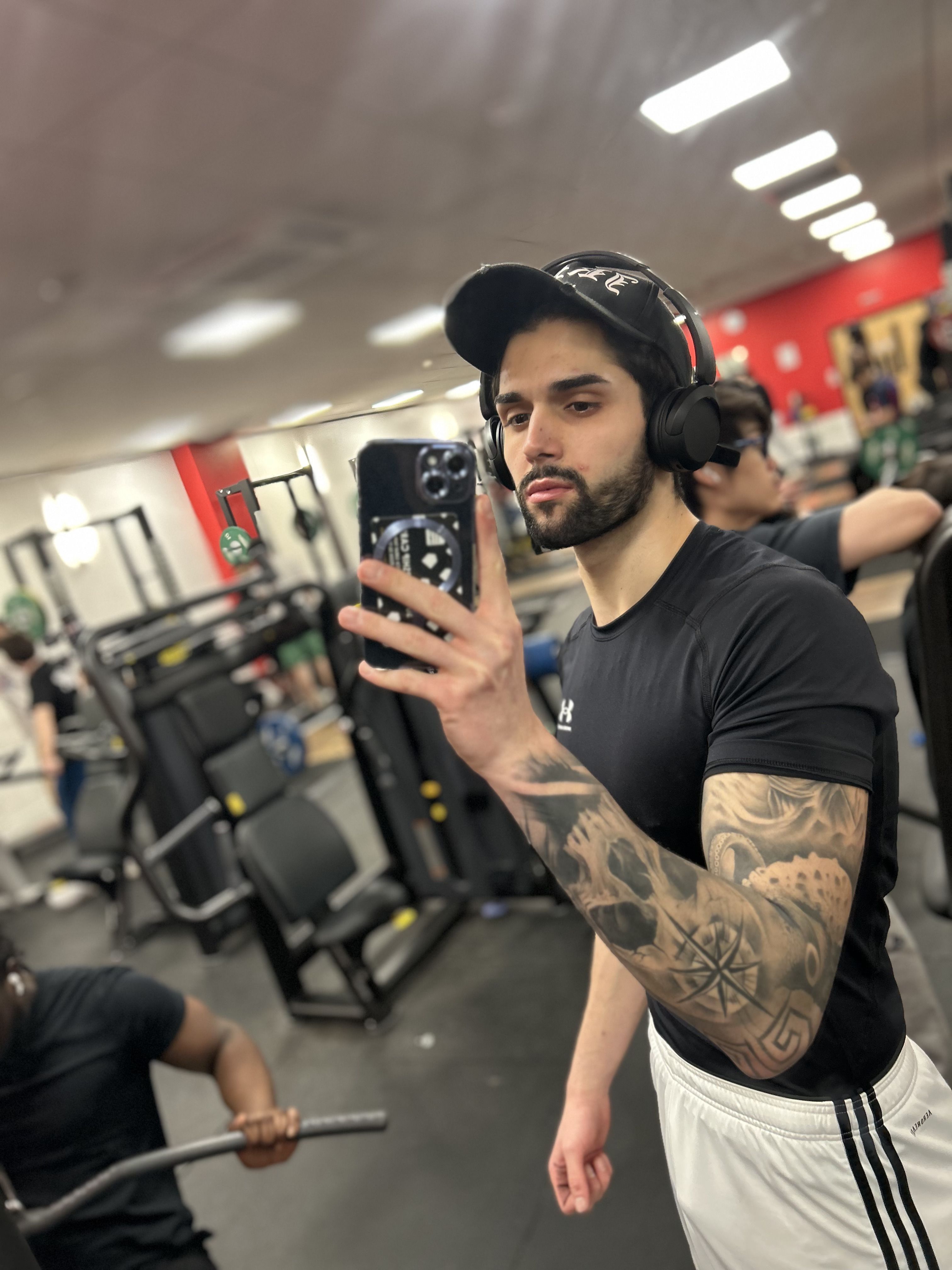 Michael taking a selfie in a mirror at the gym on campus. There are weights and gym equipment visible in the background of the image.