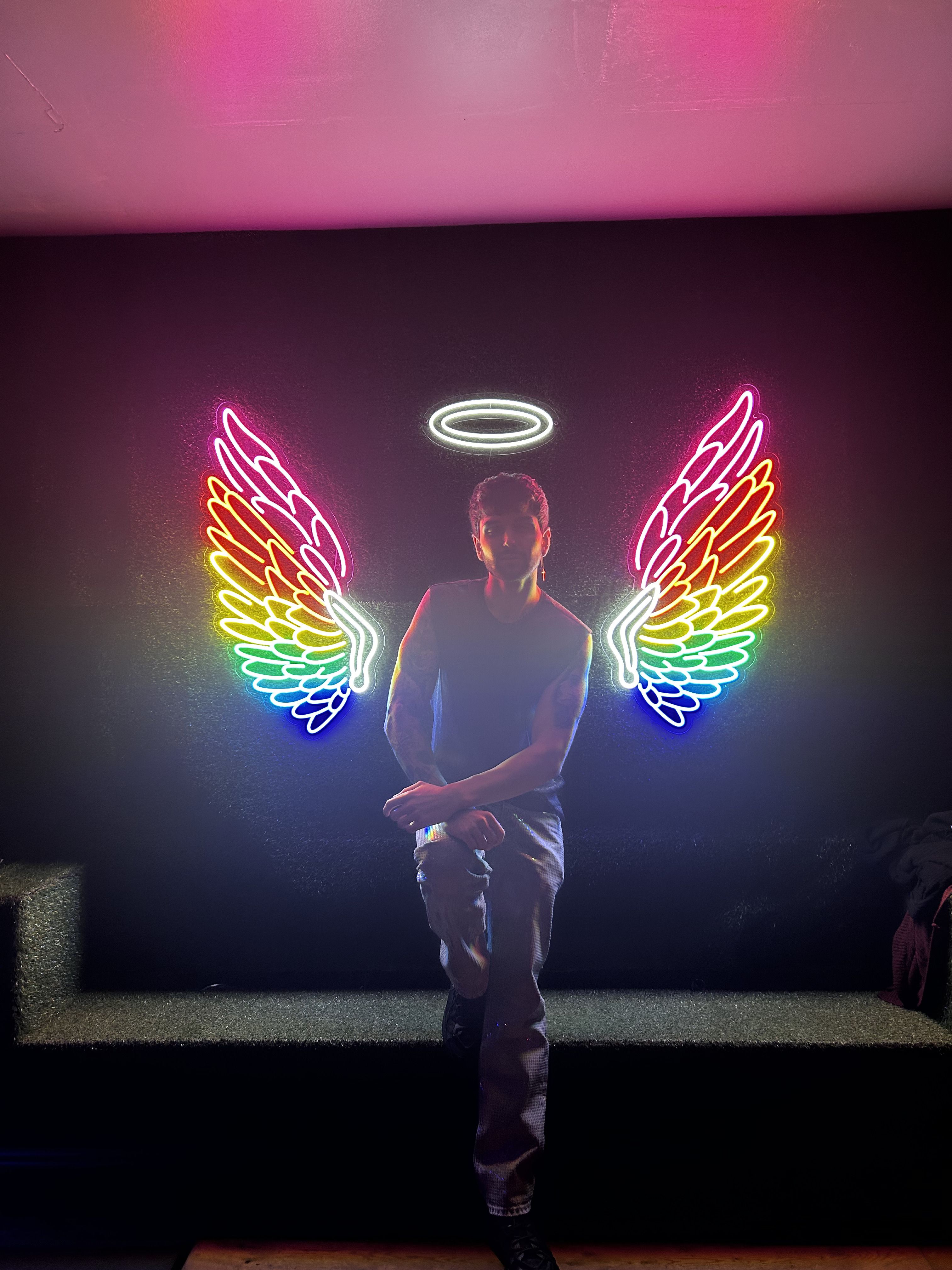 Michael stood in front of rainbow coloured illuminated wings with a white halo above his head